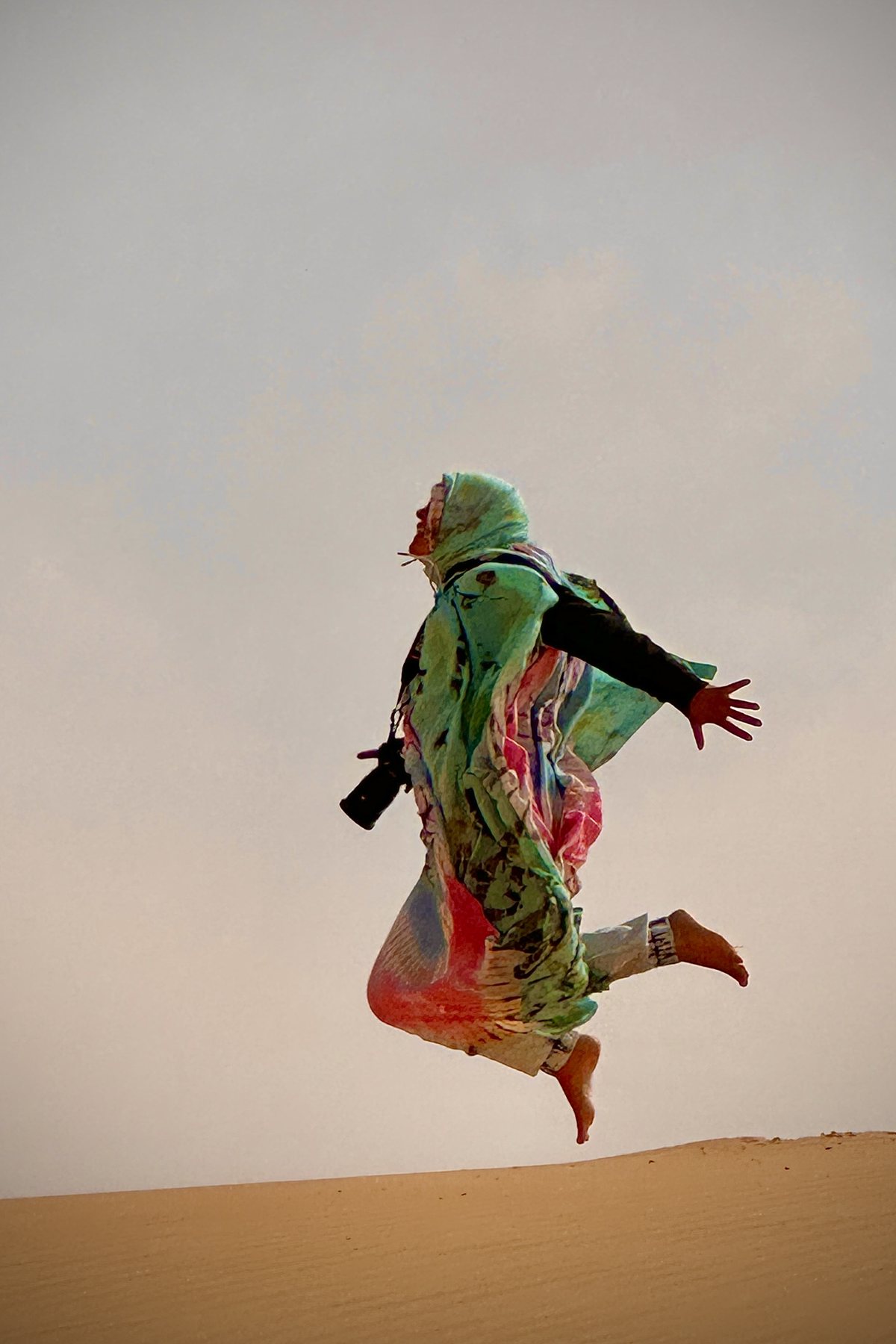 Susi Childers jumping on a sand dune with her camera